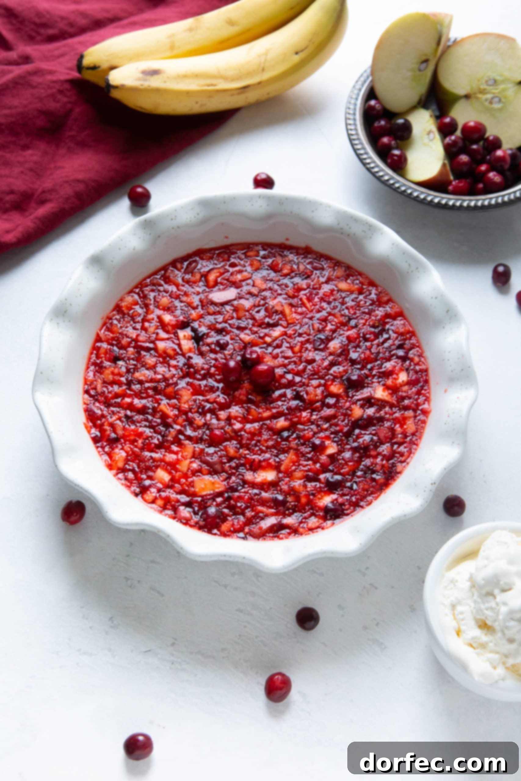 A white ceramic pie dish filled with red, fruit-infused Jell-O, garnished with three fresh cranberries in the center.