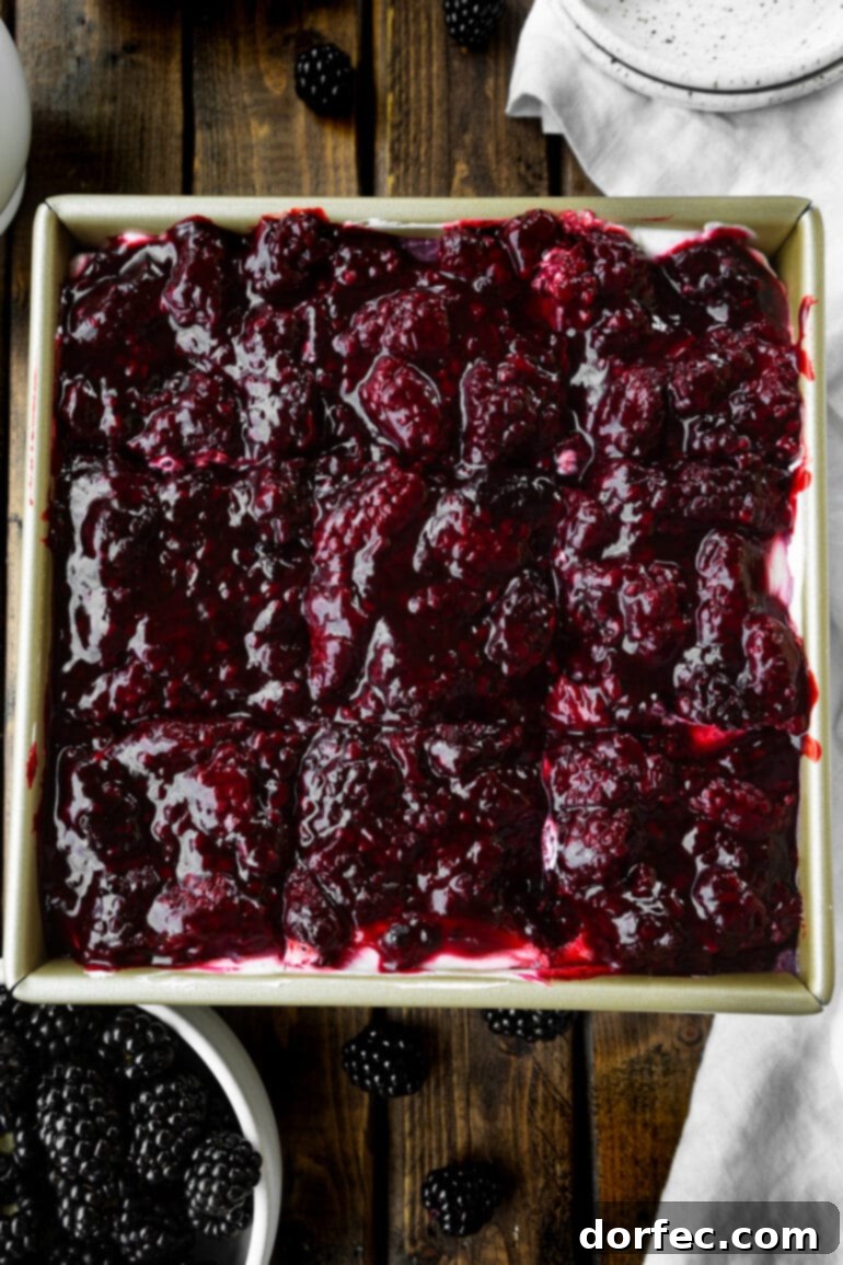 A cross-section view of Berries and Cream Cheesecake Bars, revealing a thick, golden pie crust, a rich, white cream cheese layer, and a glistening topping of bright mixed berries.