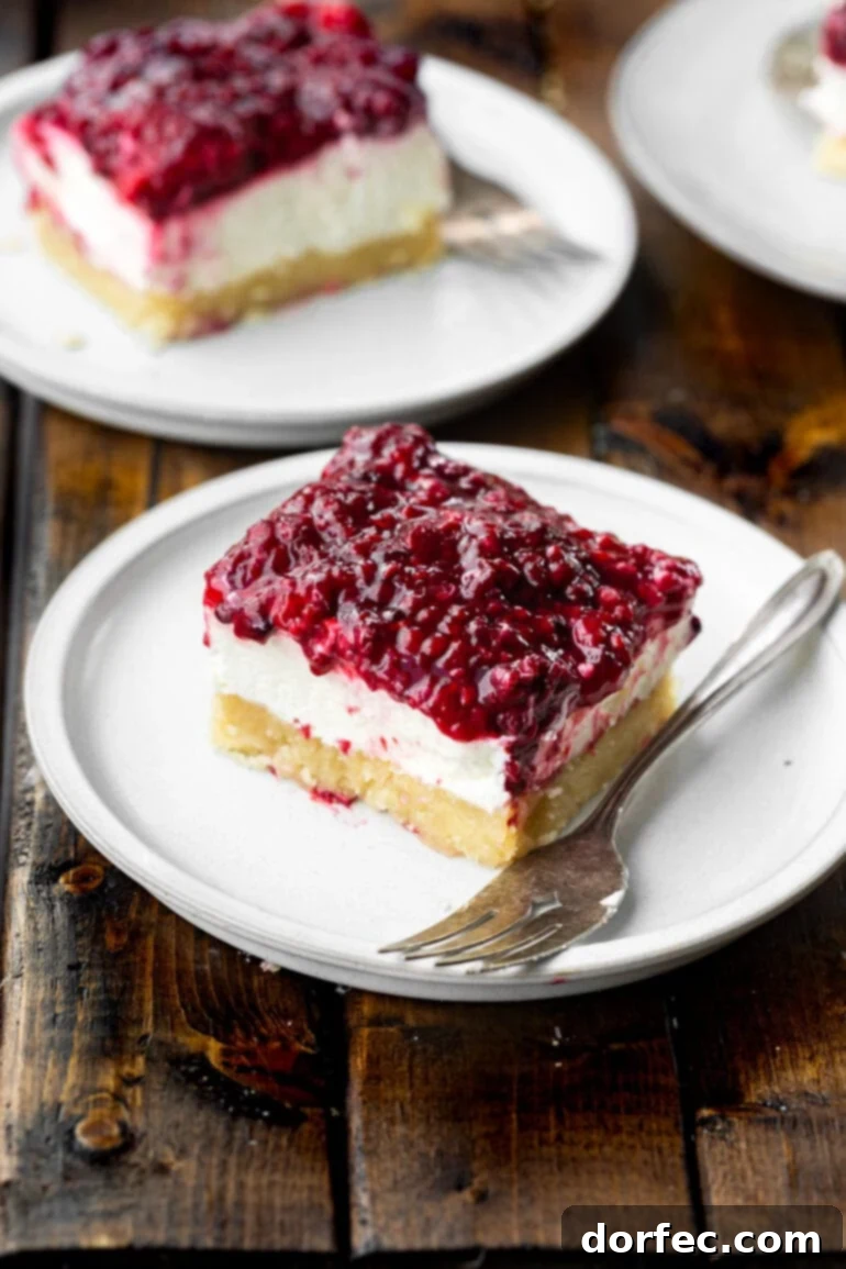 A single Berries and Cream Cheesecake Bar rests on a small white dessert plate, a fork positioned elegantly beside it, inviting a taste.