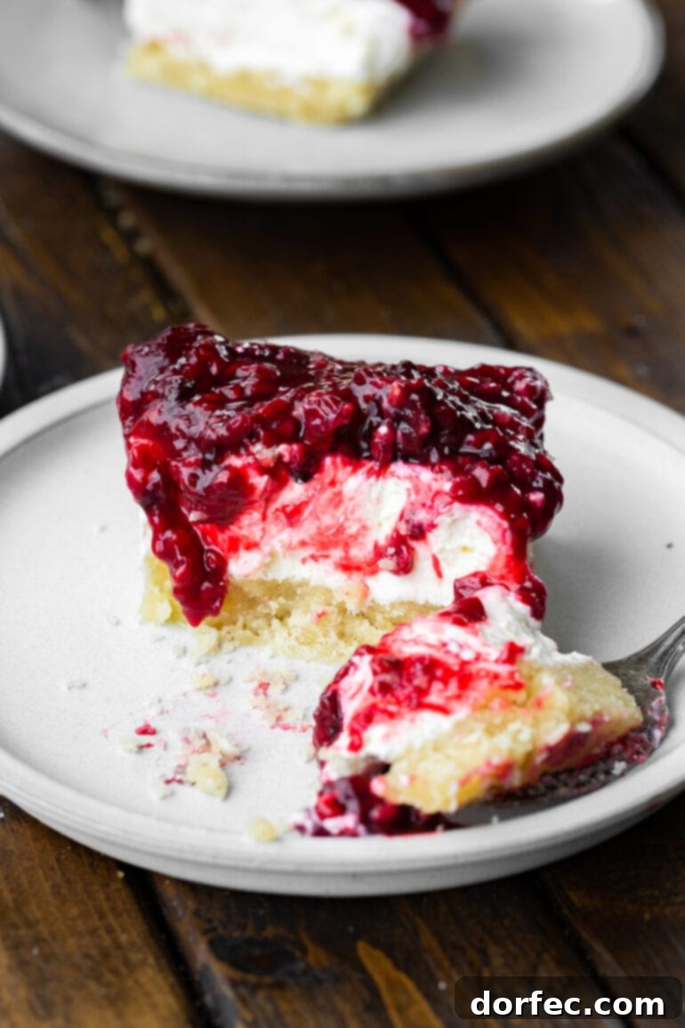 A fork gently lifts a perfect bite from a Berries and Cream Cheesecake Bar, sitting on a white dessert plate, showcasing its delightful layers.