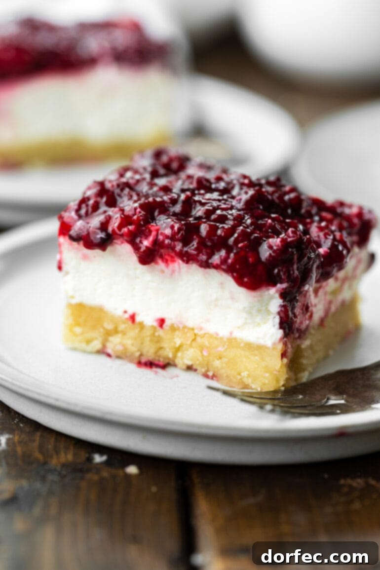 A close-up of a Berries and Cream Cheesecake Bar, highlighting the crumbly pie crust, the rich, creamy white layer, and the glistening mixed berry topping.