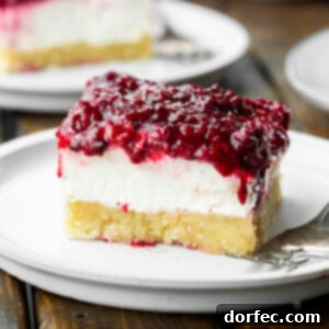 A square image of a berries and cream cheesecake bar, featuring a pie crust, creamy filling, and berry topping.