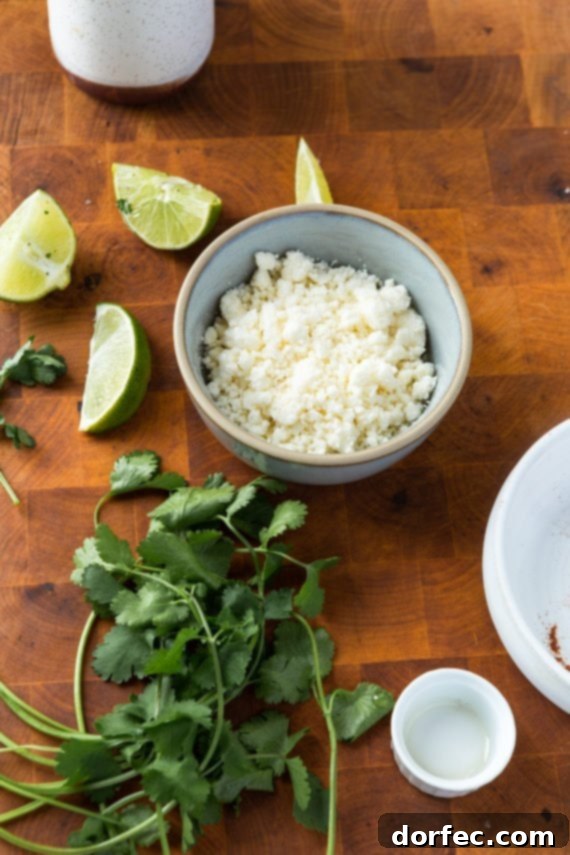 A curated selection of fresh garnishes: a bunch of bright green cilantro, several lime wedges, and a small bowl of crumbled queso fresco, all artfully arranged on a wooden cutting board, ready to finish the roasted zucchini.
