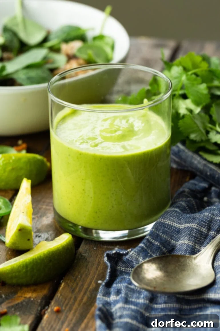 A glass jar filled with bright green avocado cilantro lime dressing, garnished with fresh lime wedges and cilantro sprigs.