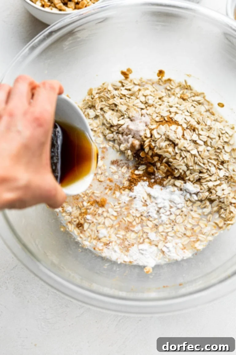 Baked Apple Fritter Oatmeal Delight 2 A photo of vanilla extract being poured into a large bowl filled with uncooked oats and milk, showcasing the mixing process for the baked oatmeal.