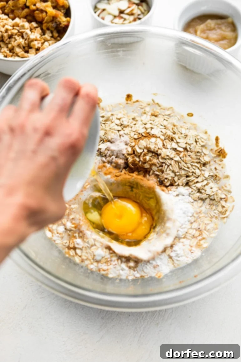 Baked Apple Fritter Oatmeal Delight 3 A photo of two eggs being cracked and poured into a bowl containing the pre-mixed ingredients for apple fritter baked oatmeal.