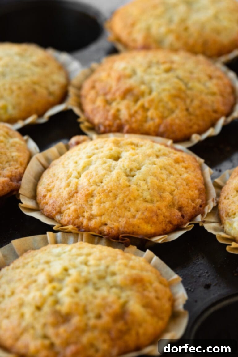 Several perfectly golden brown baked banana muffins in neutral paper liners, arranged on a cooling rack.