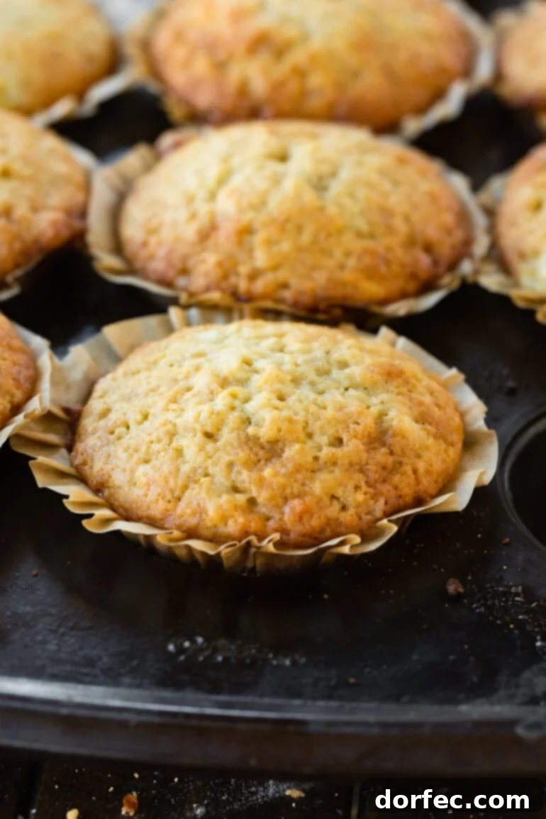 A close-up of a golden baked banana muffin with its liner slightly peeled, showcasing its soft, delicious interior.