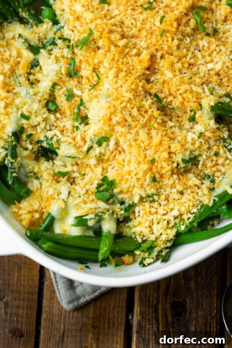 A photo of a white ceramic casserole dish containing green beans topped with a creamy sauce and a golden panko topping, ready to serve.