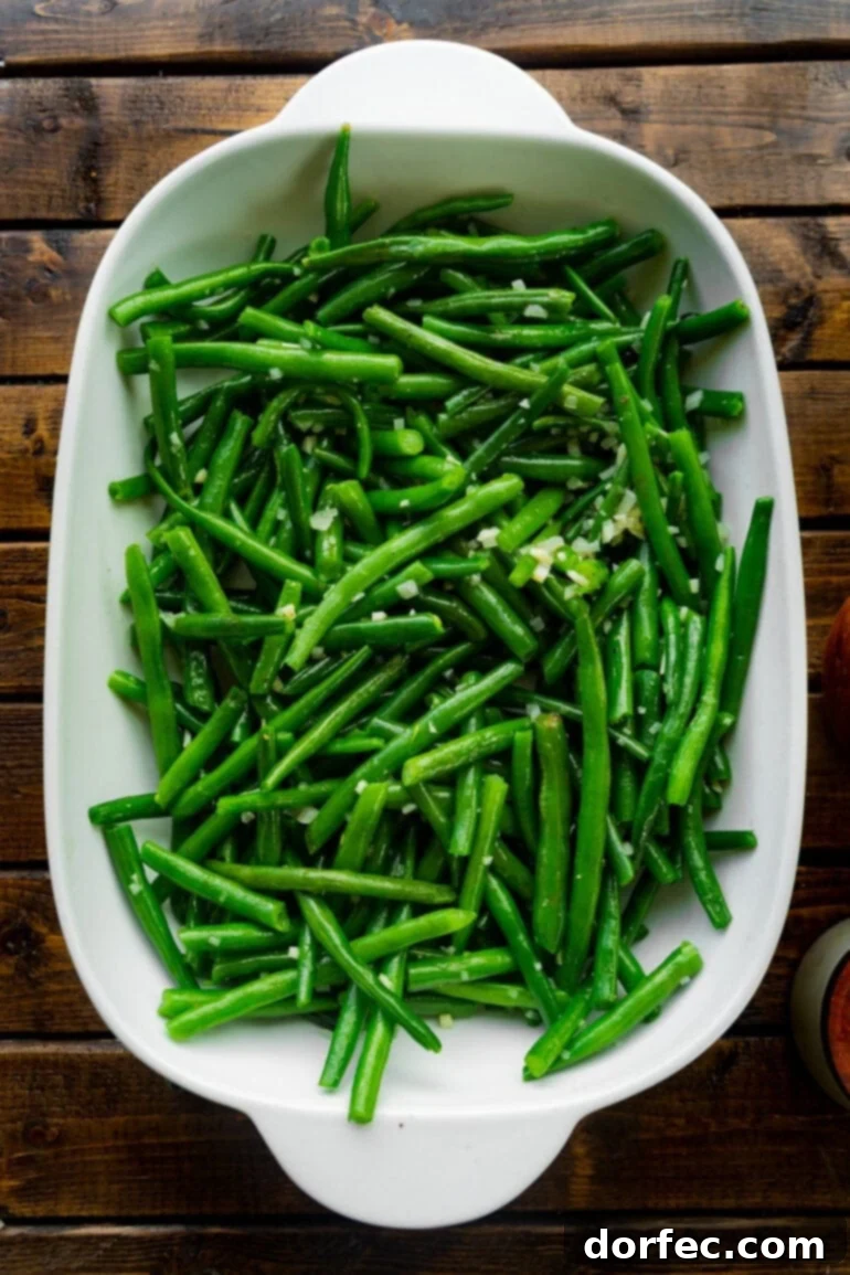A close-up photo of a casserole dish filled with bright green fresh green beans mixed with minced shallots, waiting for the creamy sauce.