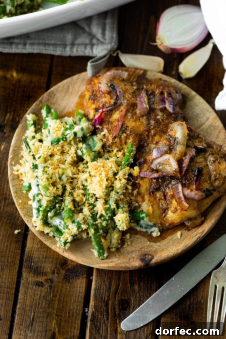 A photo of a wooden plate with two roasted chicken thighs next to a serving of creamy ranch green beans topped with crunchy golden panko.
