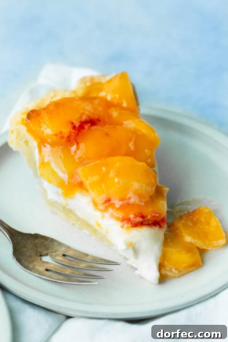 A beautiful slice of peaches and cream pie, showcasing layers of golden-brown flaky crust, rich cream, and vibrant, juicy peach slices on top. This peach pie is a perfect summer dessert.