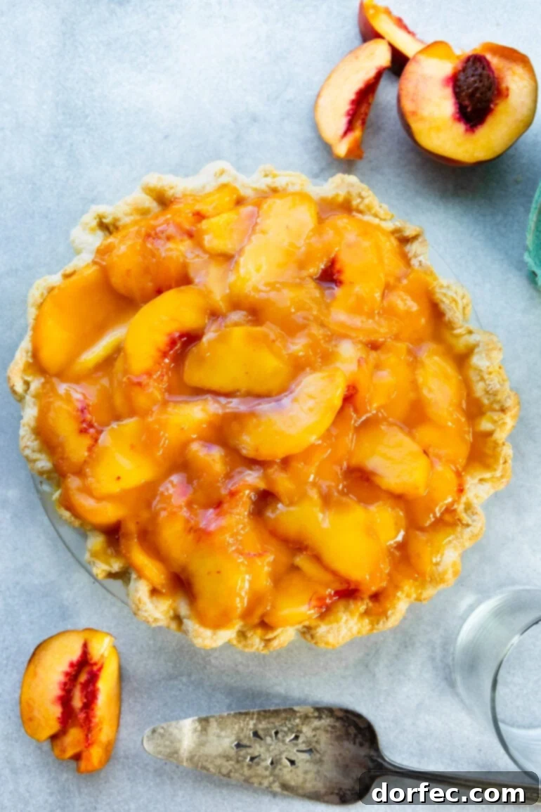 A whole, beautifully baked peaches and cream pie, featuring a golden, crimped homemade crust filled with a creamy layer and topped with a glistening arrangement of sweet, sliced peaches. An ideal summer dessert.