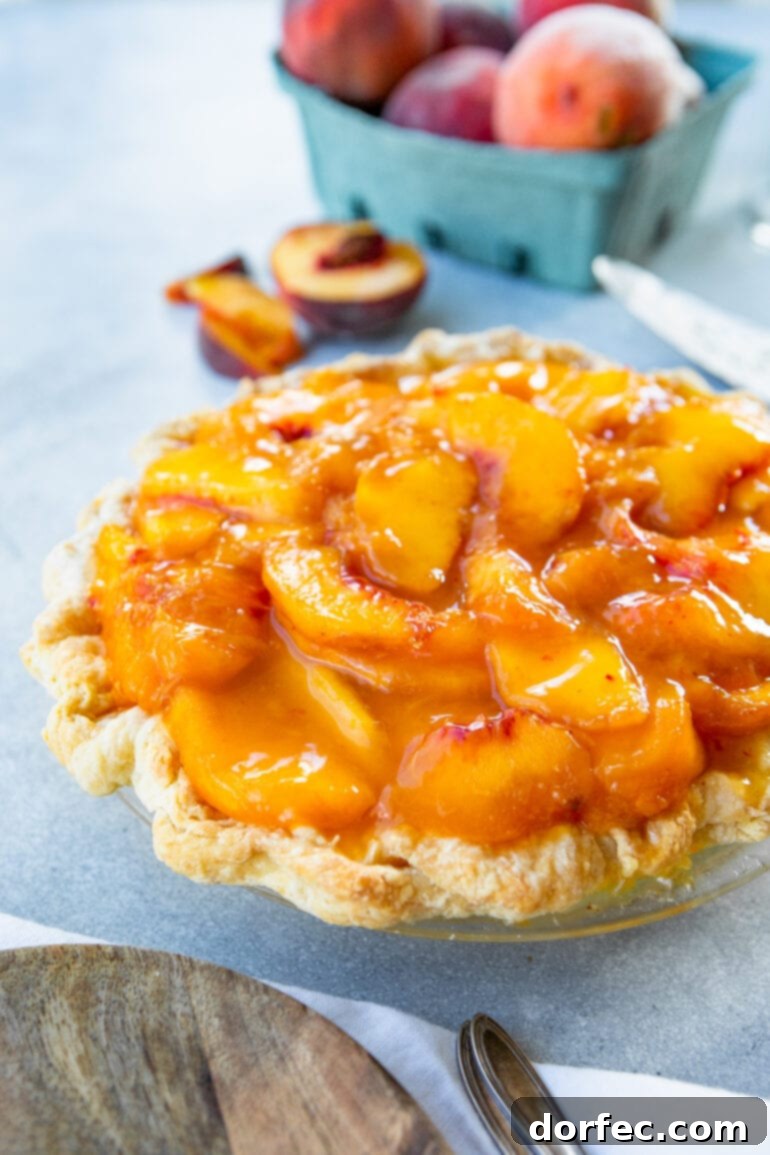 A stunning whole peach pie, featuring a rustic golden homemade crust. The pie is generously topped with a rich, saucy layer of ripe peaches resting on a creamy white base. This dessert is perfect for summer gatherings.