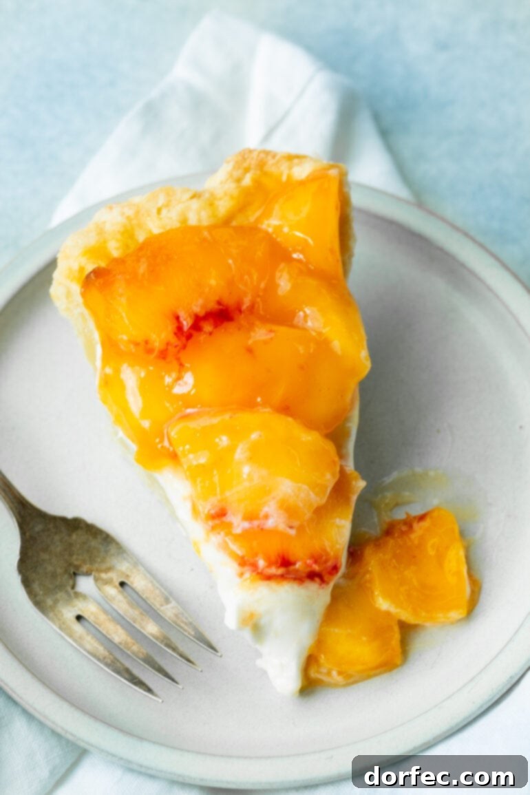 An overhead view of a single slice of peaches and cream pie, showcasing its beautiful layers. A flaky golden crust holds a creamy white filling, generously topped with glistening, juicy peach slices. This peach dessert is visually appealing and delicious.