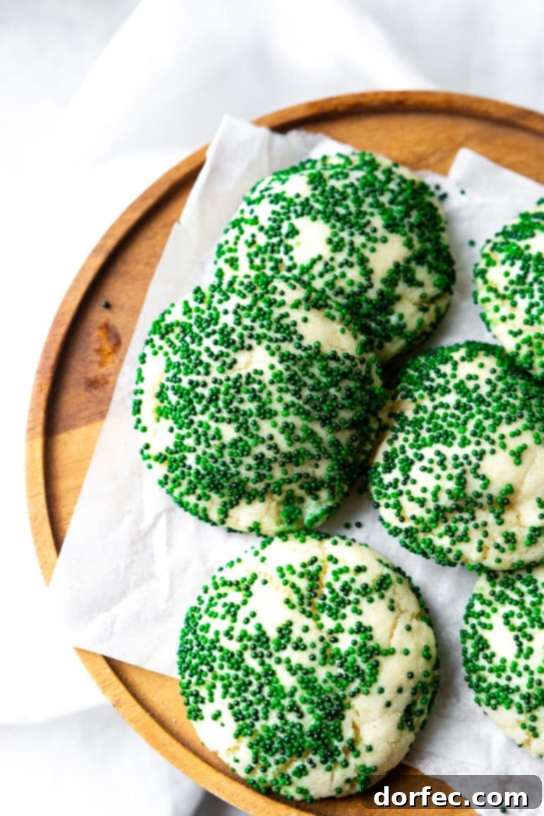 a photo of several thick and soft sugar cookies sitting on a piece of white parchment paper on top of a wooden serving tray. the cookies are all coated in dark green sprinkles.