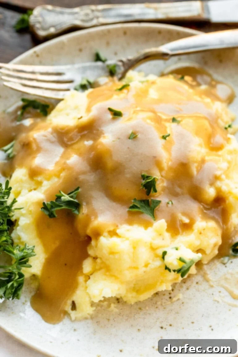A photo of creamy mashed potatoes on a dinner plate, generously topped with rich brown turkey gravy and a sprinkle of fresh herbs.