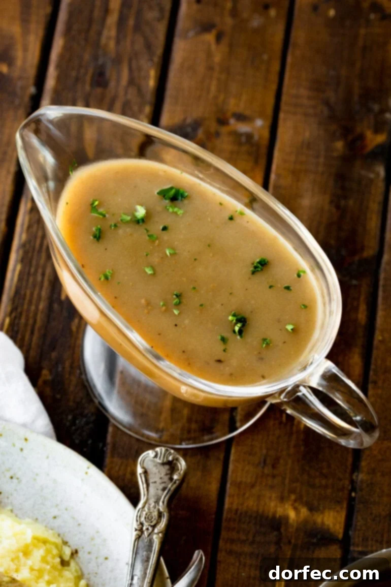 A photo of a clear glass gravy boat filled to the brim with smooth, rich turkey gravy, garnished with a sprinkle of chopped fresh parsley.