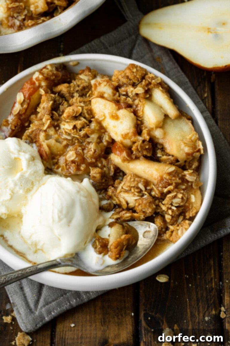 A bowl of golden pear crisp, generously topped with two scoops of creamy vanilla ice cream, and a spoon ready to dig in.
