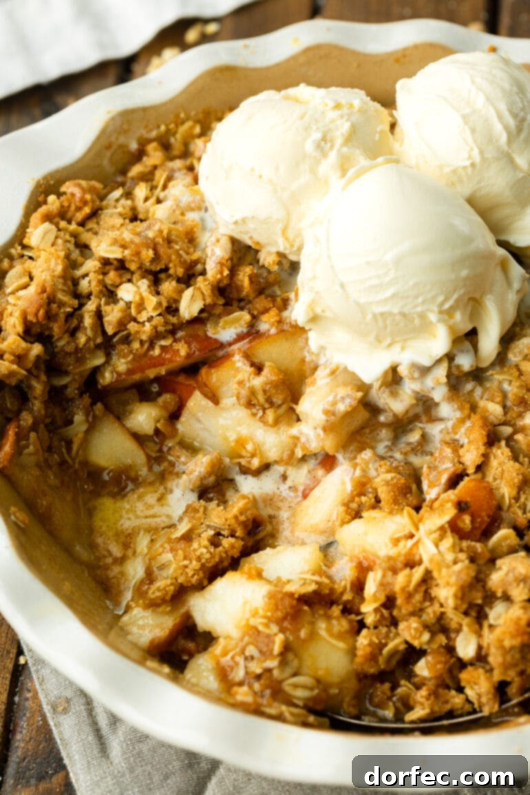 A round baking dish filled with baked pear crisp, served warm with melting scoops of vanilla ice cream, and a portion already scooped out.