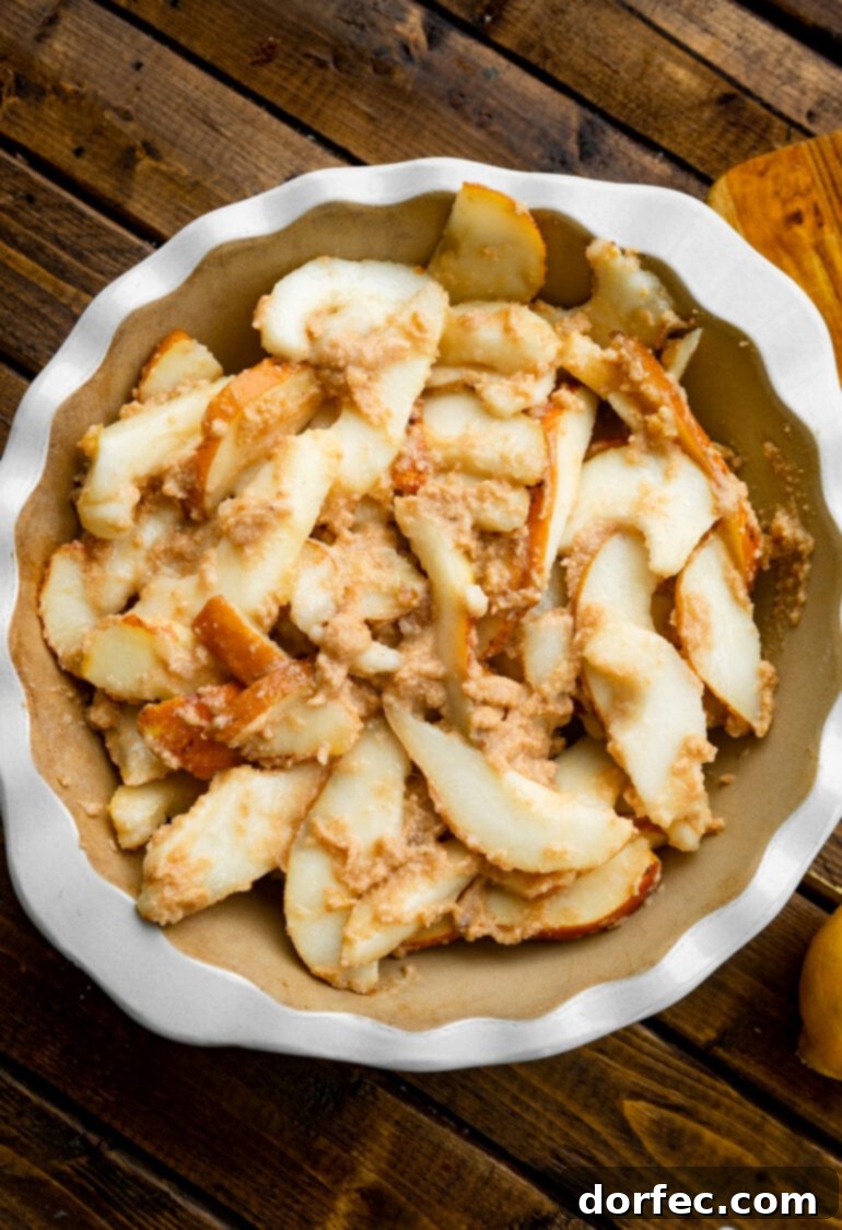 A deep pie dish filled with beautifully sliced pears, coated in a buttery, cinnamon-spiced mixture, ready for the topping.