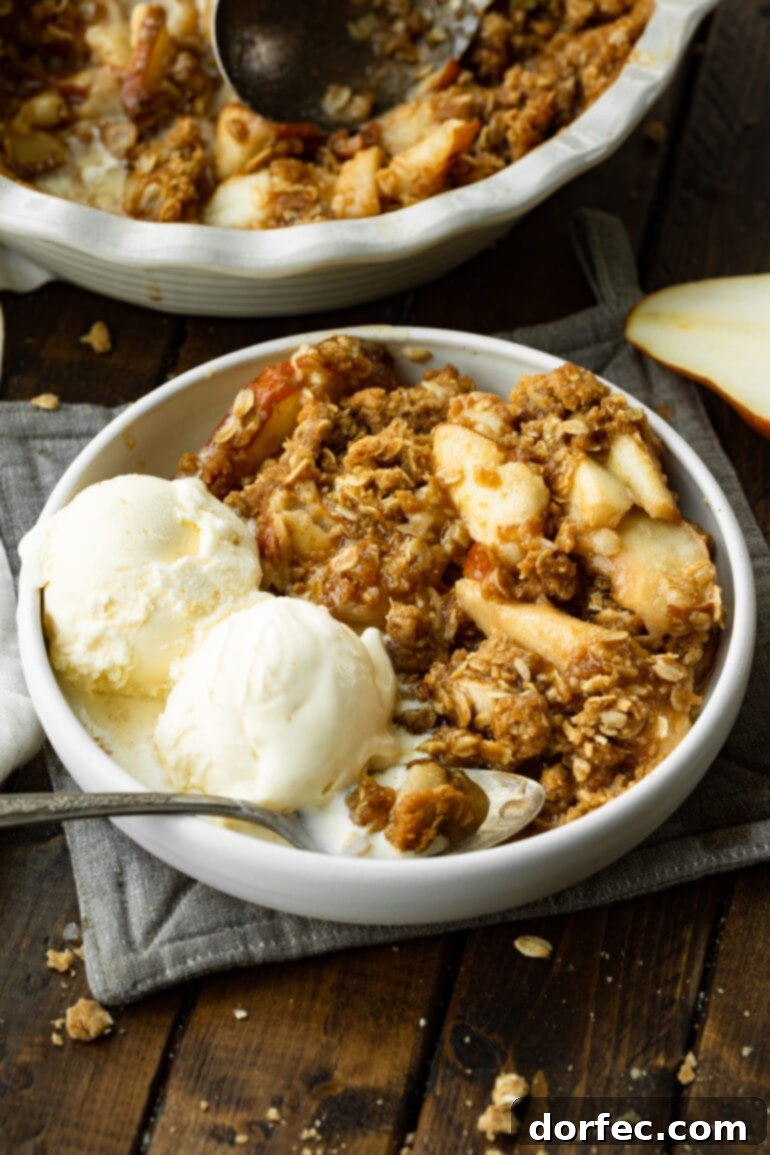A white bowl filled with a warm pear crisp, topped with two scoops of vanilla ice cream, ready to be enjoyed as a comforting dessert.