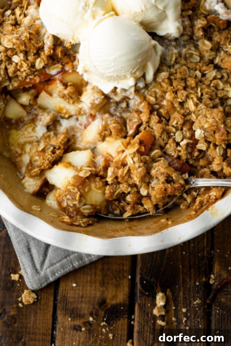 A person scooping a warm serving of pear crisp from a circular baking dish, showcasing the tender fruit and crunchy topping.