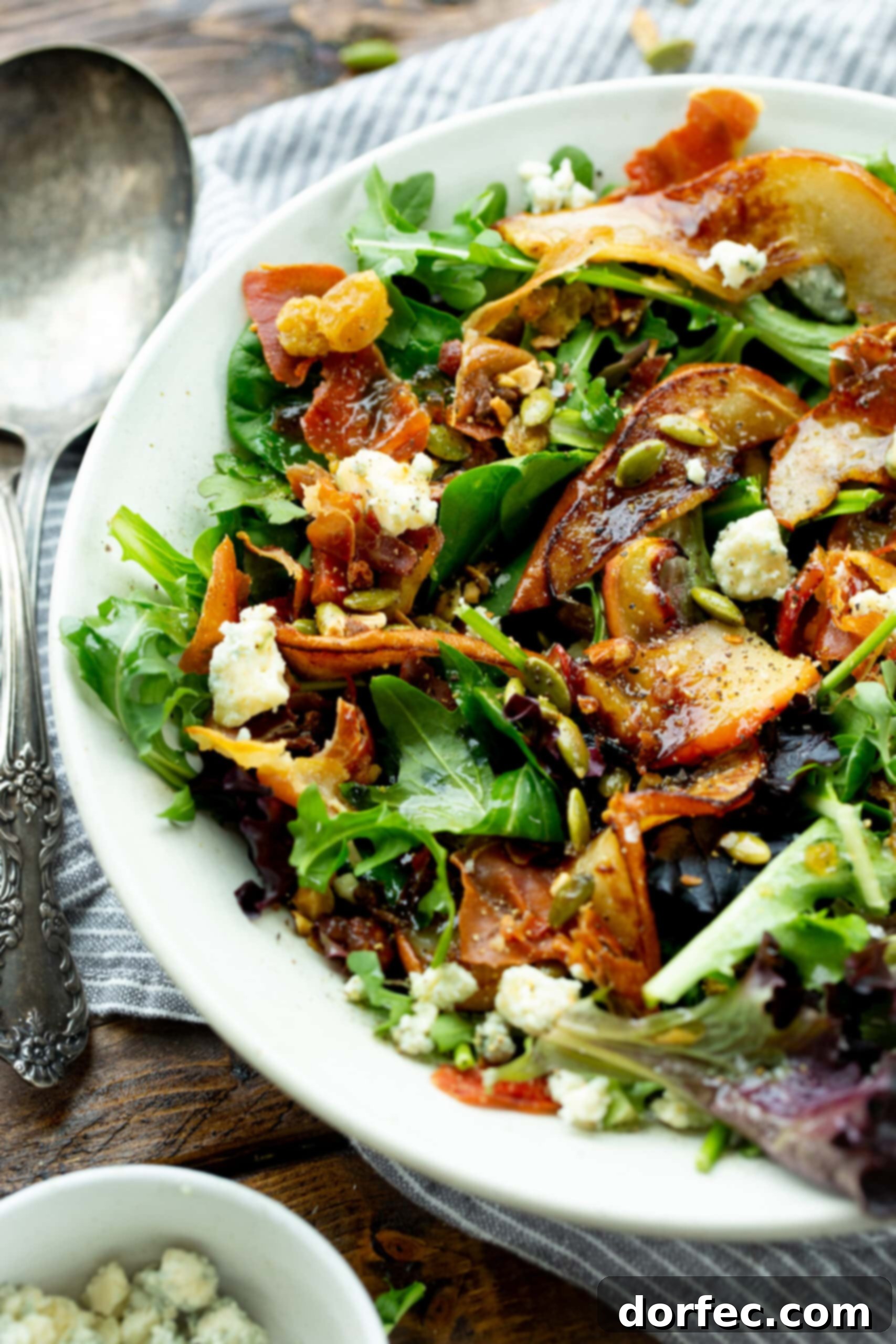 Gourmet Roasted Pear & Apple Salad with Caramelized Shallot Maple Vinaigrette A large white plate topped with a vibrant roasted apple and pear salad, featuring mixed greens, prosciutto, cinnamon pecans, pepitas, gorgonzola, and raisins, drizzled with a rich vinaigrette.