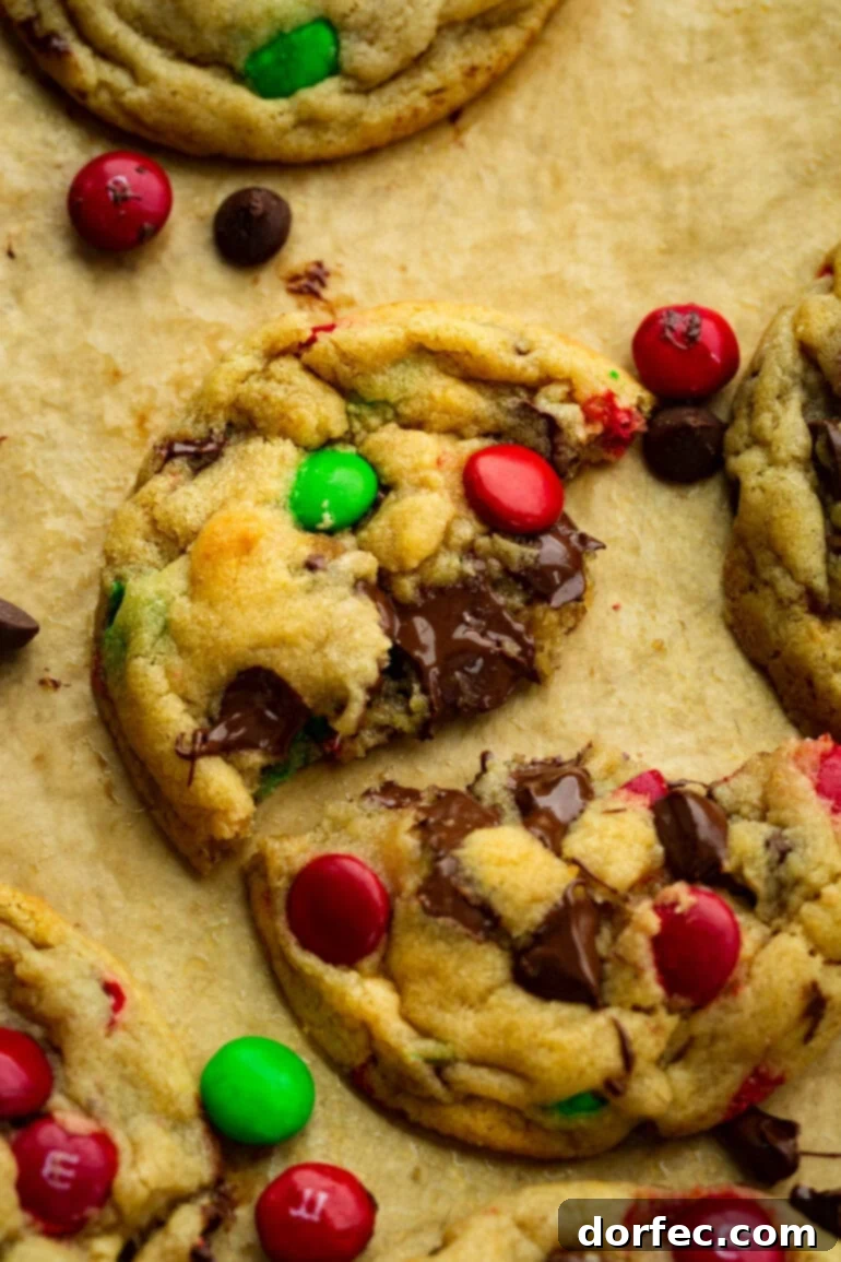 A golden-baked Christmas M&M chocolate chip cookie, broken in half to reveal its soft, gooey, and irresistible chocolatey center with colorful M&M pieces.