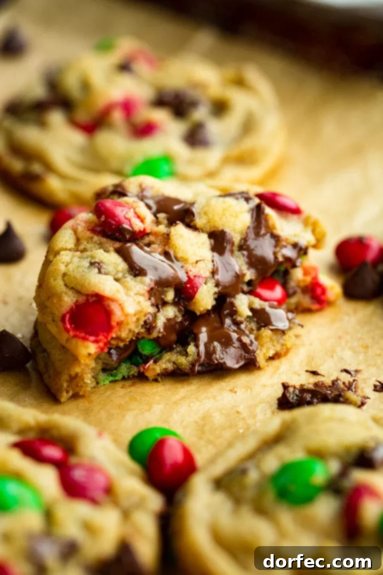 A delectable stack of thick, chewy Christmas M&M chocolate chip cookies, broken in half to showcase their gooey, melted chocolate interior and vibrant holiday colors.