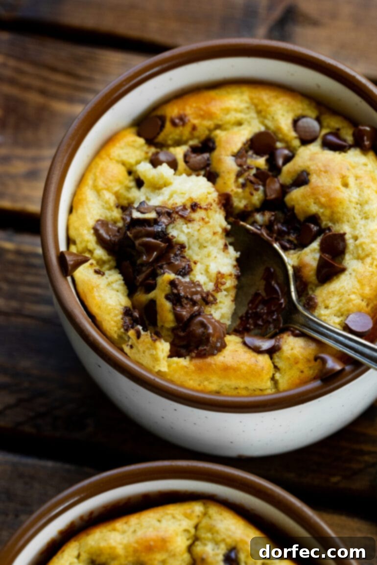 Chocolate Chip Protein Mug Oatmeal 5 A photo looking over a spoon as it scoops a bite from a mug filled with golden baked oatmeal, topped with mini chocolate chips, highlighting the texture.