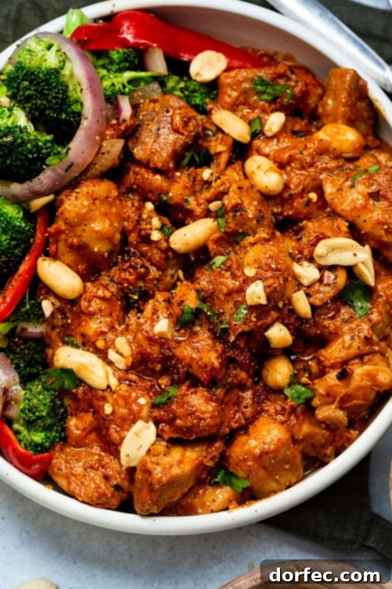 A photo of a large white bowl full of saucy peanut butter chicken, garnished with chopped peanuts and fresh cilantro.