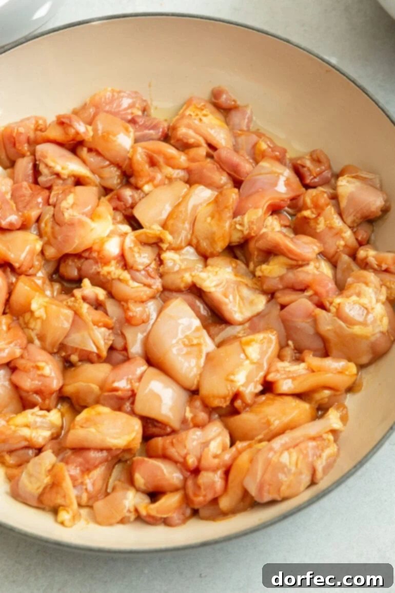 A photo of a bowl filled with uncooked chicken thigh chunks marinating in soy sauce, ready for cooking.