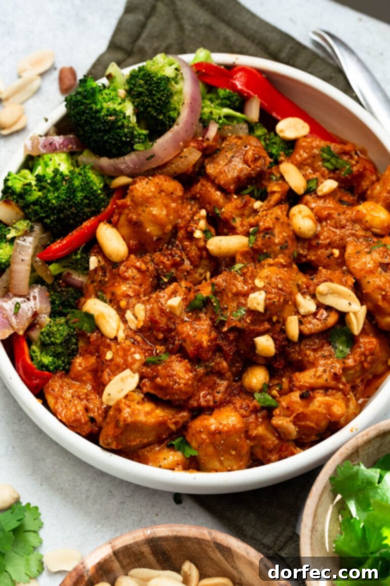 A photo of a large bowl filled with peanut butter chicken, accompanied by a vibrant broccoli salad on the side, and garnished with peanuts and cilantro.