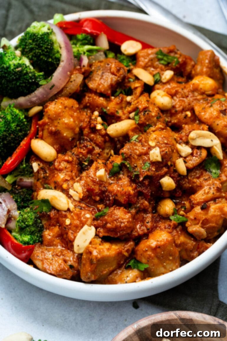 A photo of a serving of peanut butter chicken, topped with fresh cilantro and chopped peanuts, presented with a side of broccoli salad.