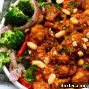 A photo of saucy peanut butter chicken, generously topped with chopped peanuts, served alongside vibrant broccoli, thinly sliced red onions, and crisp red peppers.