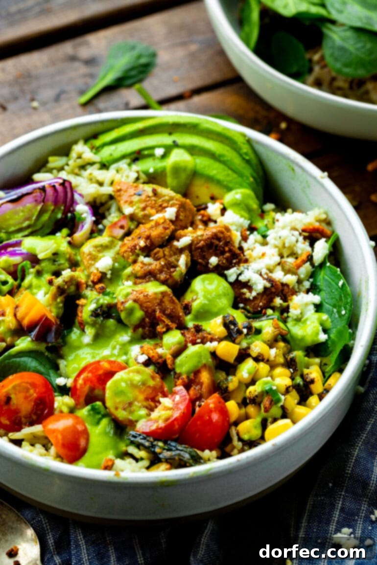 Zesty Chicken Burrito Bowl 2 A beautifully presented Mexican chicken burrito bowl, featuring a base of cilantro lime rice, savory sticky Mexican chicken, grilled corn, fresh cherry tomatoes, thinly sliced avocado, red onions, and a vibrant green creamy avocado dressing.