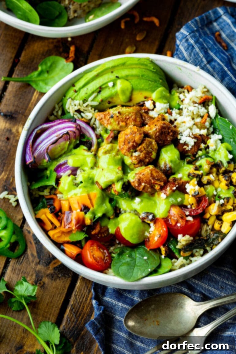 Zesty Chicken Burrito Bowl 3 A close-up photo of a vibrant Mexican chicken burrito bowl, showcasing bright orange and red bell peppers, finely diced red onion, creamy avocado slices, seasoned chunks of sticky Mexican chicken, all crowned with a fresh, green avocado creamy dressing.