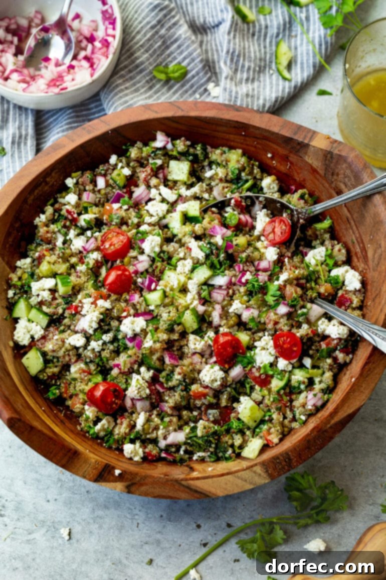 a photo of a large wooden serving bowl full of Mediterranean quinoa salad with two silver serving spoon stuck in it.