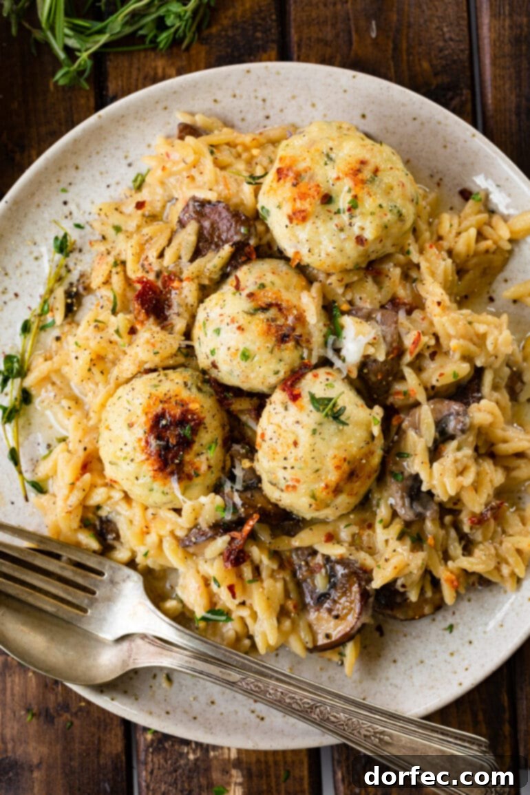 a photo of creamy mushroom orzo topped with golden herby chicken meatballs.