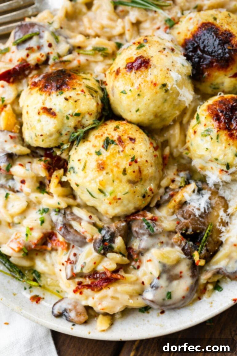 a close up photo of golden baked chicken meatballs topped with fresh herbs and on top of creamy mushroom orzo.
