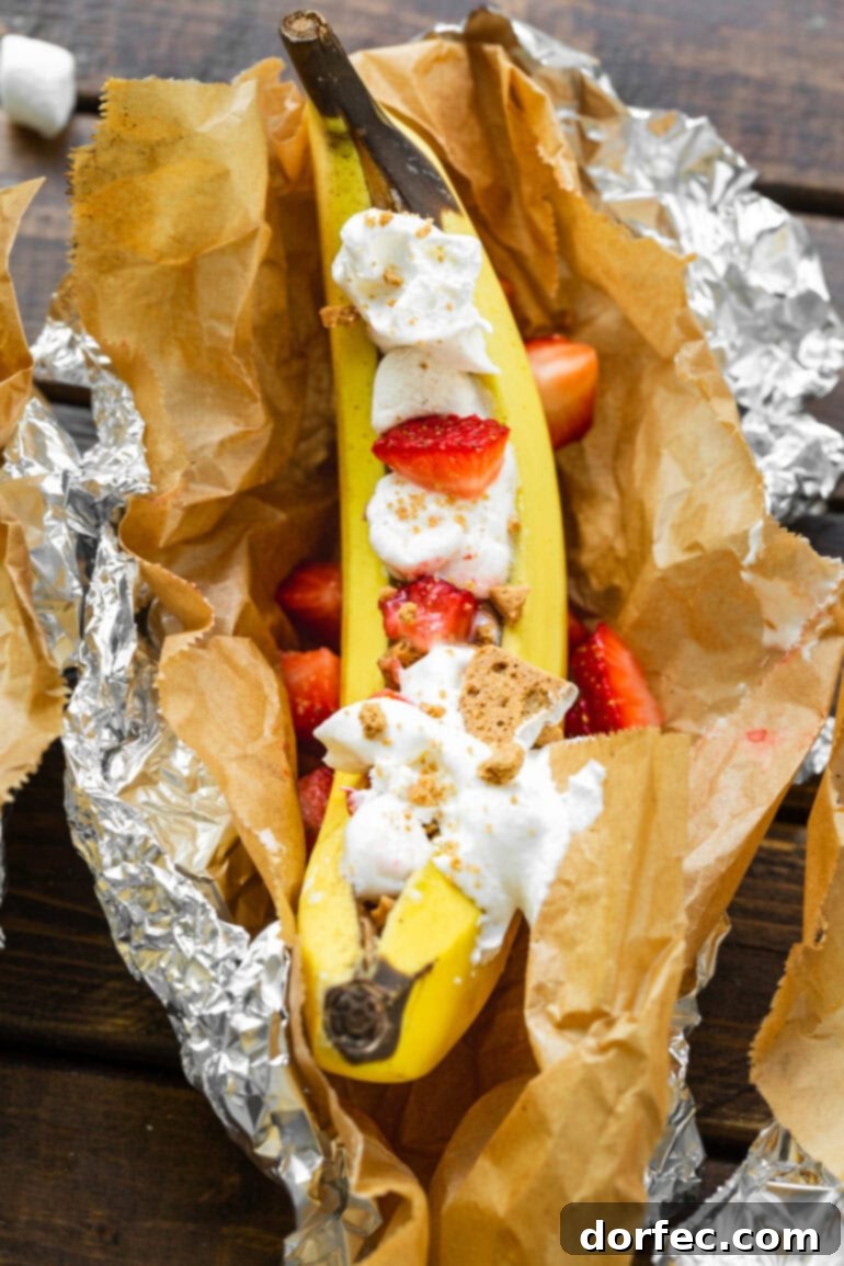 Our Favorite Campfire Banana Boats 5 A vibrant Strawberry Shortcake Banana Boat, beautifully presented in parchment paper and foil, topped with fresh strawberries, crumbled cookies, and a dollop of whipped cream.