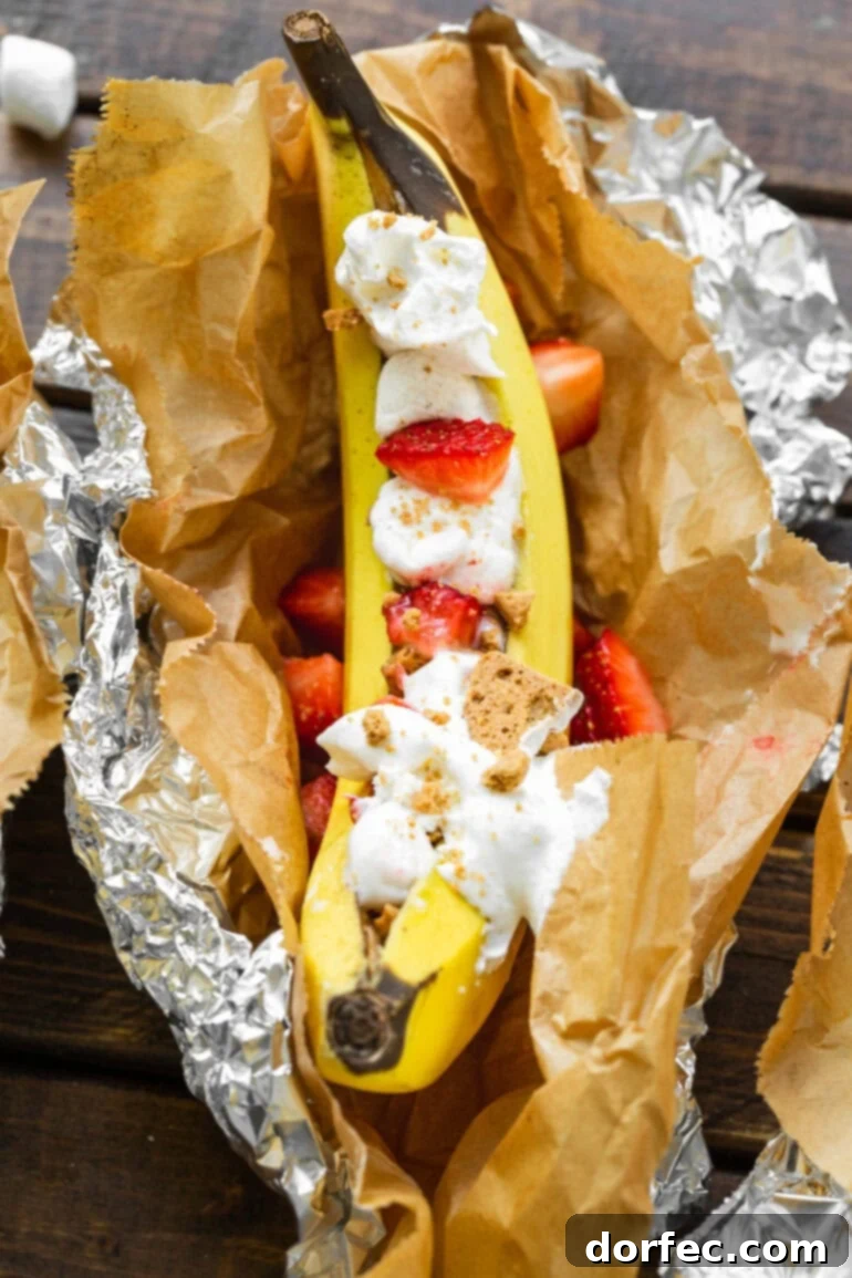 Our Favorite Campfire Banana Boats 10 A delightful Strawberry Shortcake Banana Boat, elegantly nestled in parchment paper and foil, showcasing its fresh fruit and cookie toppings.