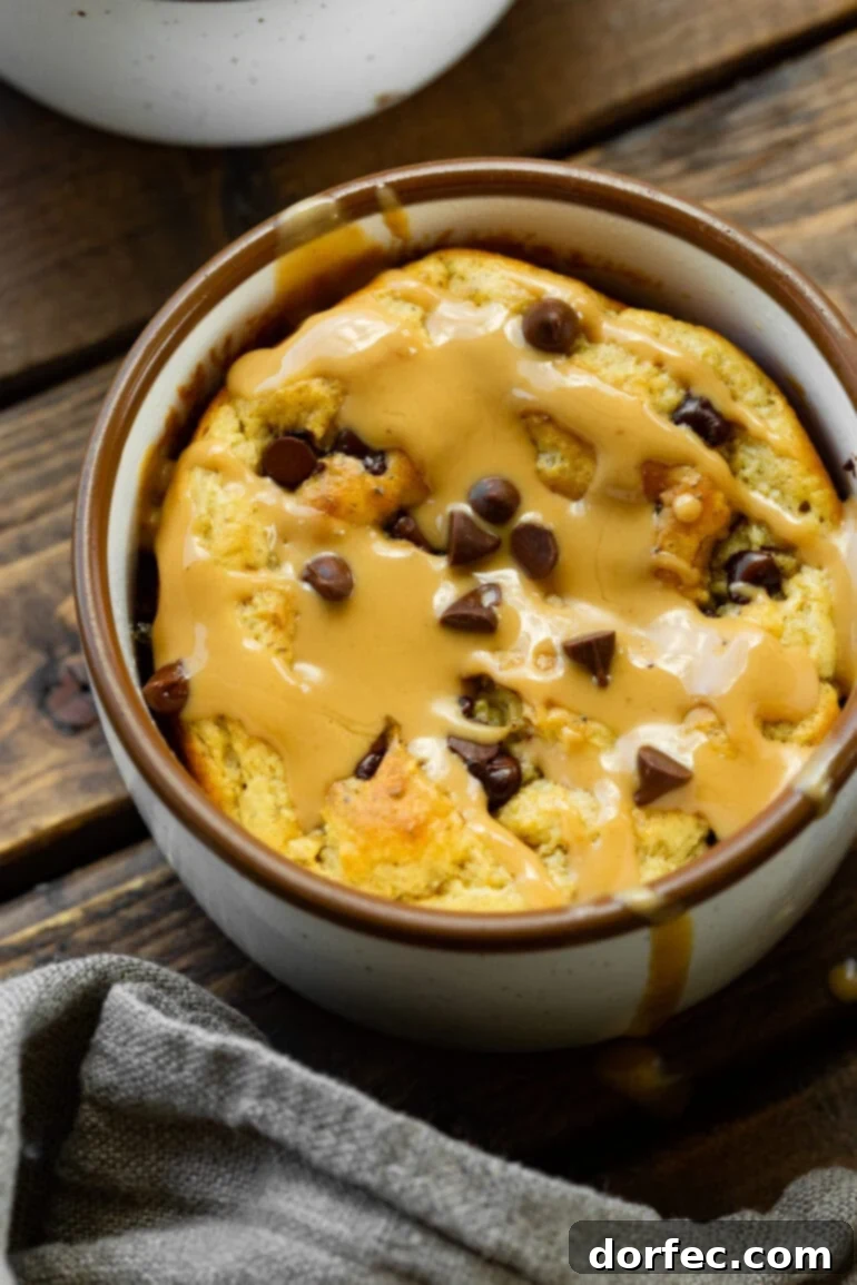 A beautifully baked oatmeal mug cake, generously topped with mini chocolate chips and a luscious drizzle of hot peanut butter, ready to be enjoyed.