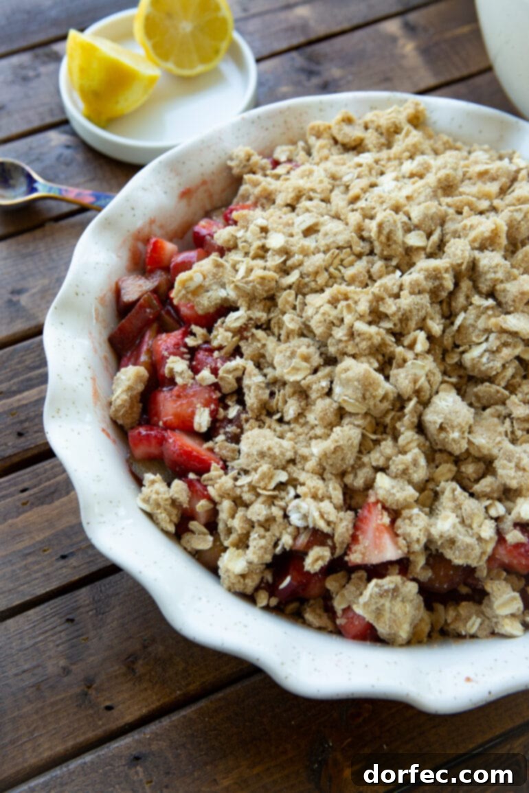 a photo of an unbaked strawberry rhubarb crisp topped with chunky buttery oat topping.