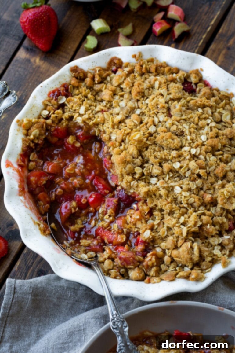 a photo of a strawberry rhubarb crisp in a round baking dish and a serving missing so you can see the juice red filling and the crunchy buttery oat topping.
