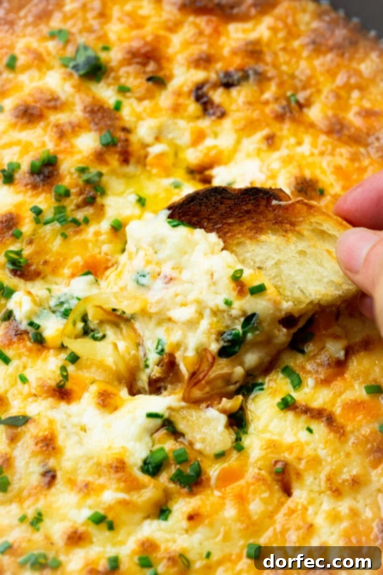 Someone scooping cheesy onion dip onto a toasted piece of bread, showcasing the creamy texture.
