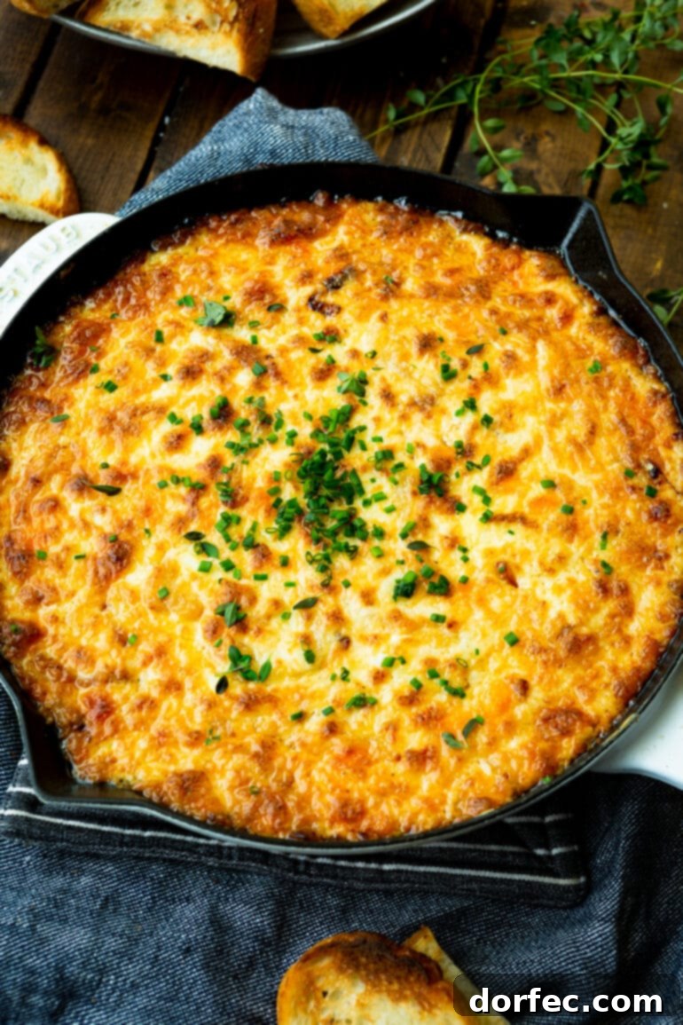 A large cast iron skillet brimming with baked cheesy onion dip, garnished generously with fresh herbs.