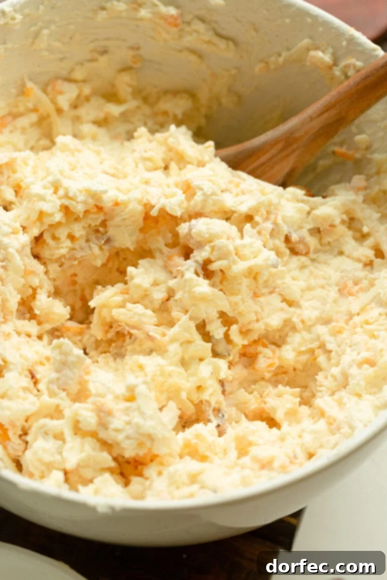 A wooden spoon stirring a creamy blend of five cheeses and caramelized onions in a cast iron skillet.