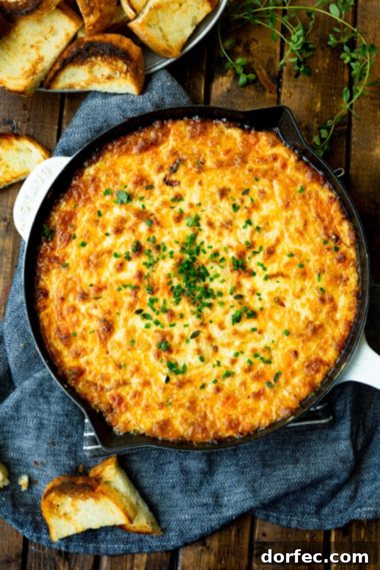 An overhead view of a cast iron skillet filled with golden baked cheesy onion dip, topped with vibrant minced chives.